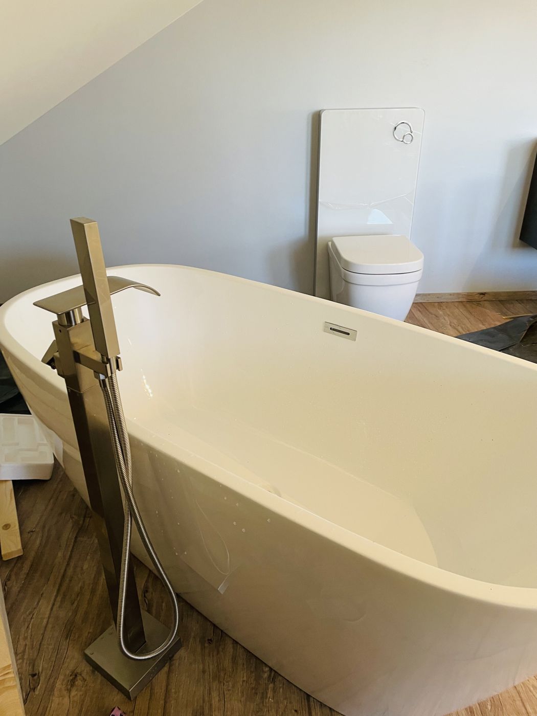 Freistehende Badewanne mit Standarmatur auf Holzoptik-Boden